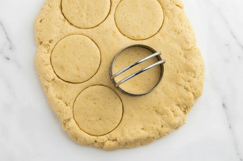 Biscuit dough with a round cutter cutting out circular shapes.